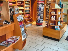 Innenansicht einer Apotheke mit Verkaufsregalen, Freiwahlartikeln und Präsentationsständern im Kundenbereich.